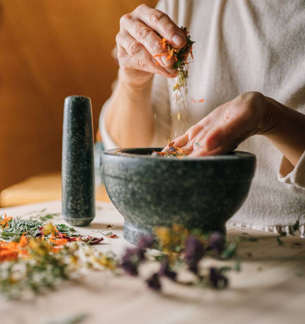 Close-up of hands grinding dried botanicals in a mortar